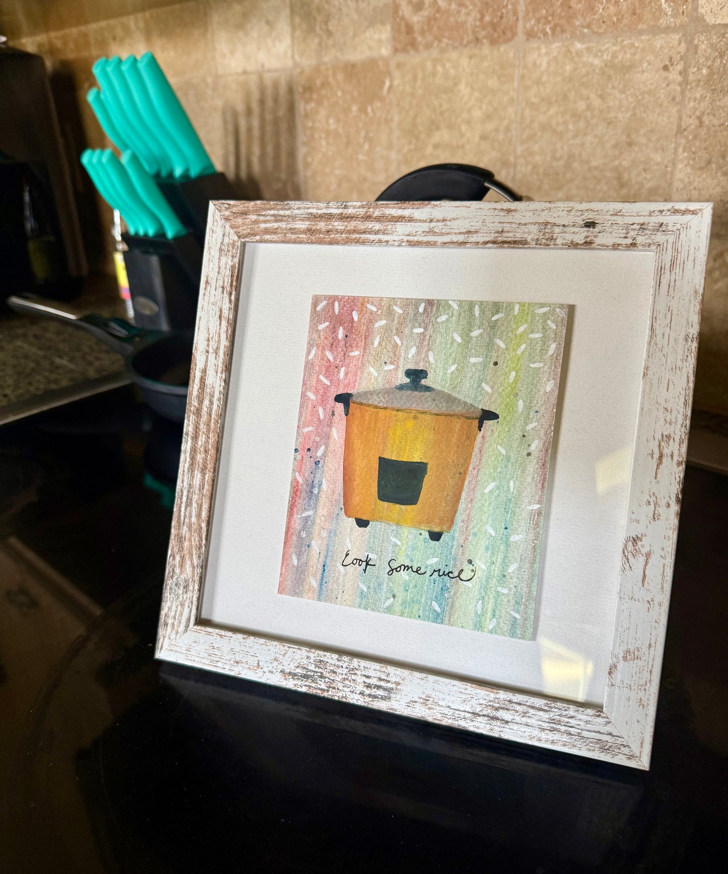Framed artwork of a bright ricepot on a kitchen counter
